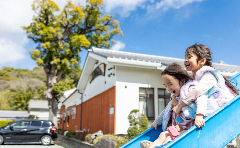 青空を背景にすべり台で遊ぶ楽しそうな様子の姉妹